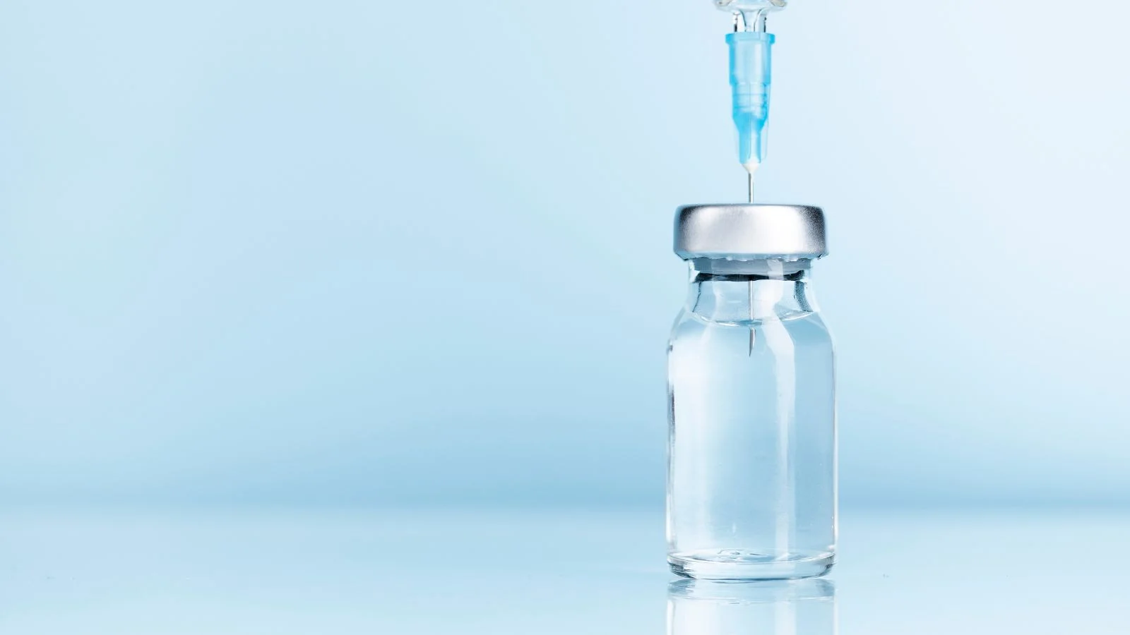 A GLP-1 medication vial with a syringe drawing a dose against a soft blue background